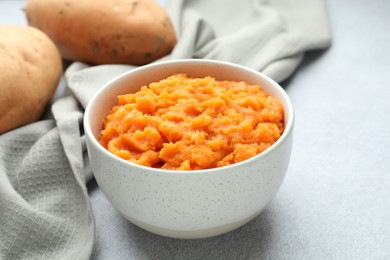 Photo of Tasty mashed sweet potato in bowl and fresh vegetables on gray table, closeup