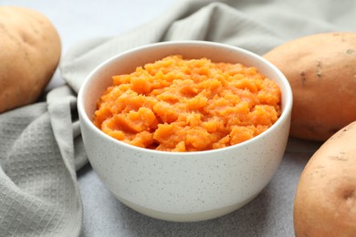 Photo of Tasty mashed sweet potato in bowl and fresh vegetables on gray table, closeup