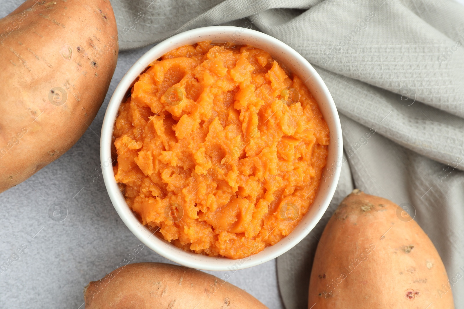 Photo of Tasty mashed sweet potato in bowl and fresh vegetables on gray table, flat lay