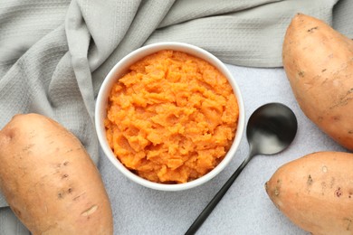 Photo of Tasty mashed sweet potato in bowl, spoon and fresh vegetables on gray table, flat lay