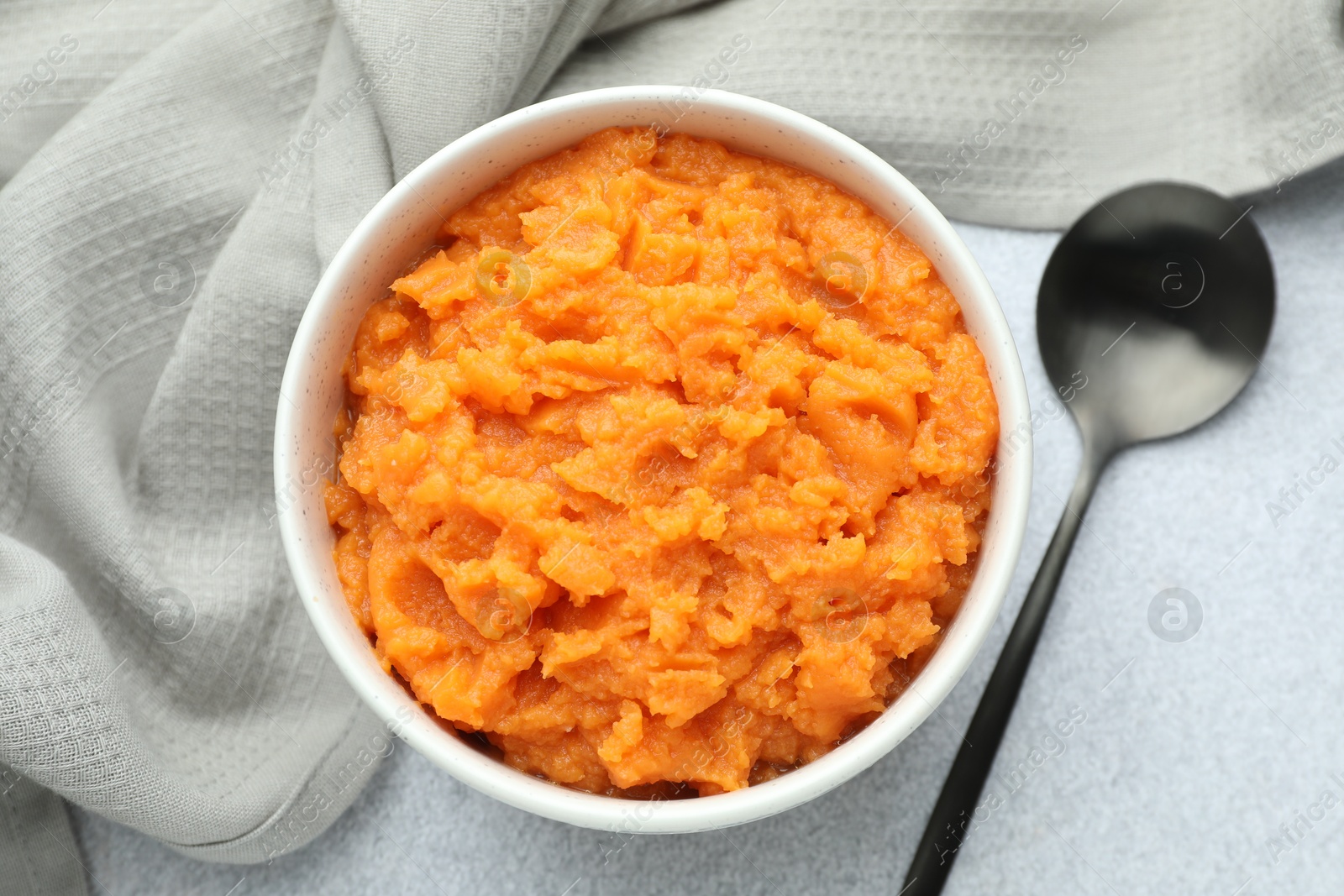 Photo of Tasty mashed sweet potato in bowl and spoon on gray table, flat lay