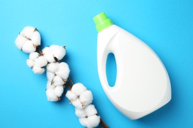 Photo of Bottle of laundry detergent and cotton flowers on blue background, flat lay