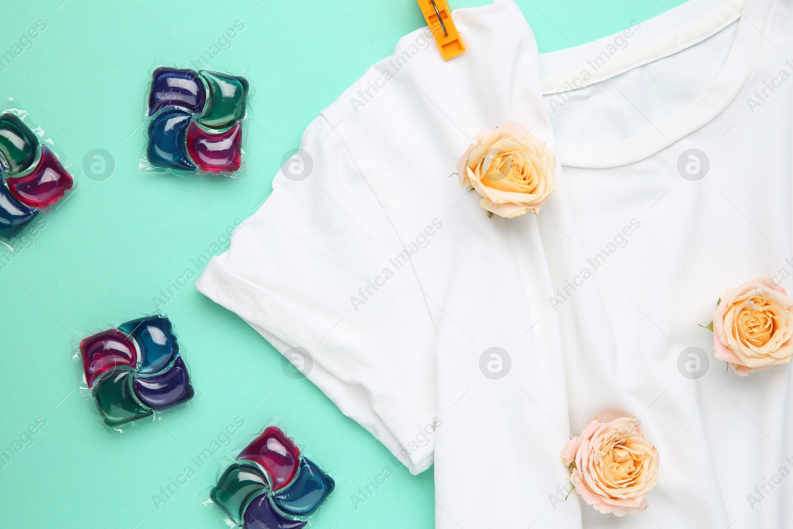 Photo of Laundry detergent pods, t-shirt, flowers and clothespins on turquoise background, flat lay