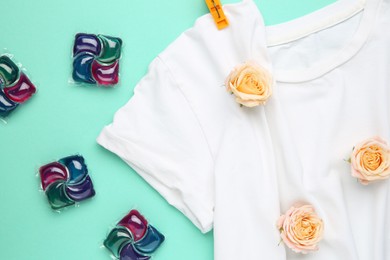 Photo of Laundry detergent pods, t-shirt, flowers and clothespins on turquoise background, flat lay