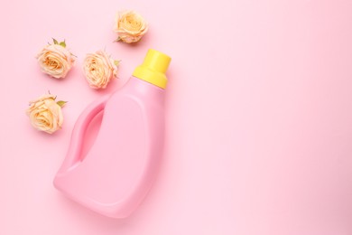 Photo of Bottle of laundry detergent and flowers on pink background, closeup. Space for text