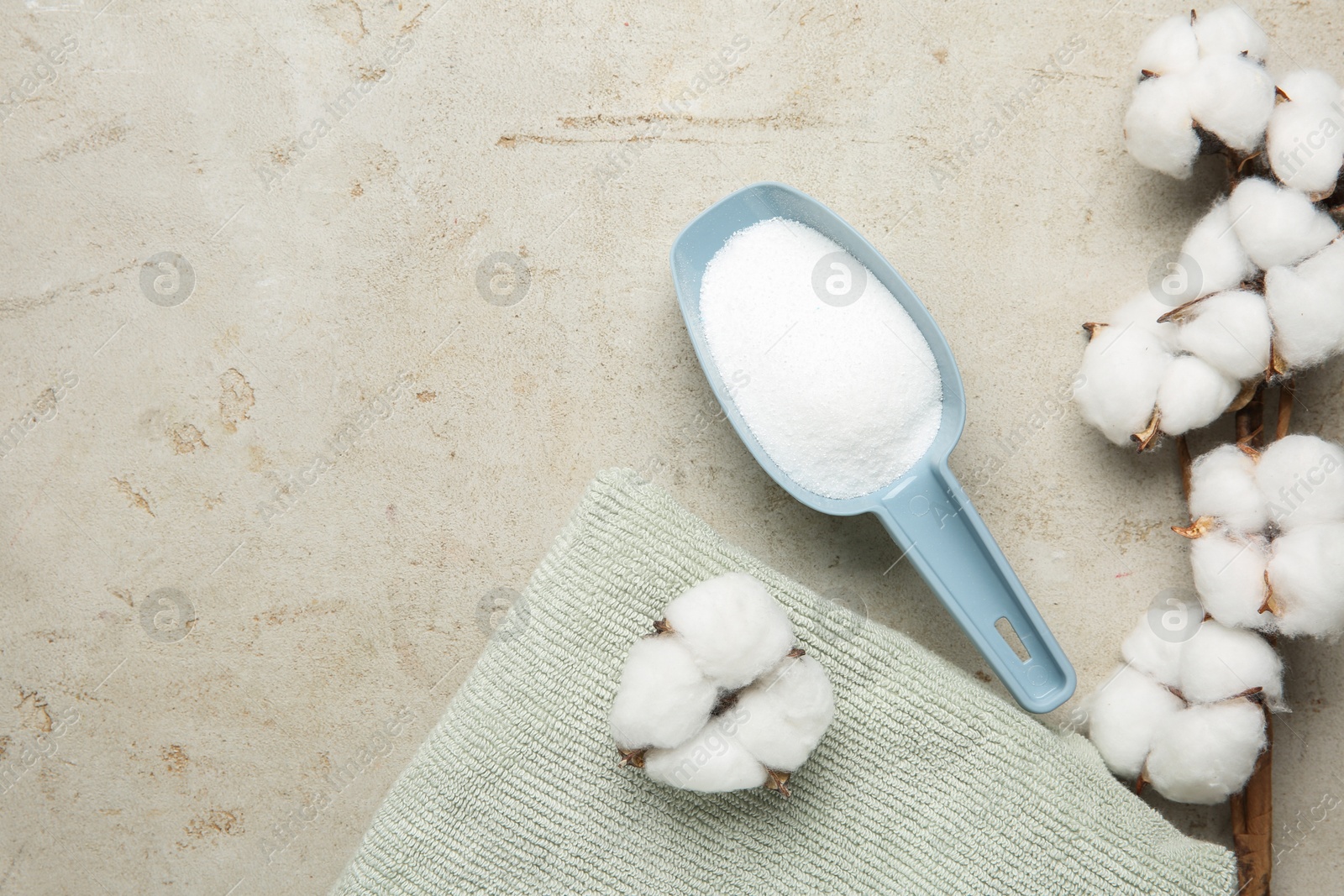 Photo of Scoop with laundry detergent, cotton flowers and towel on grey textured table, flat lay. Space for text