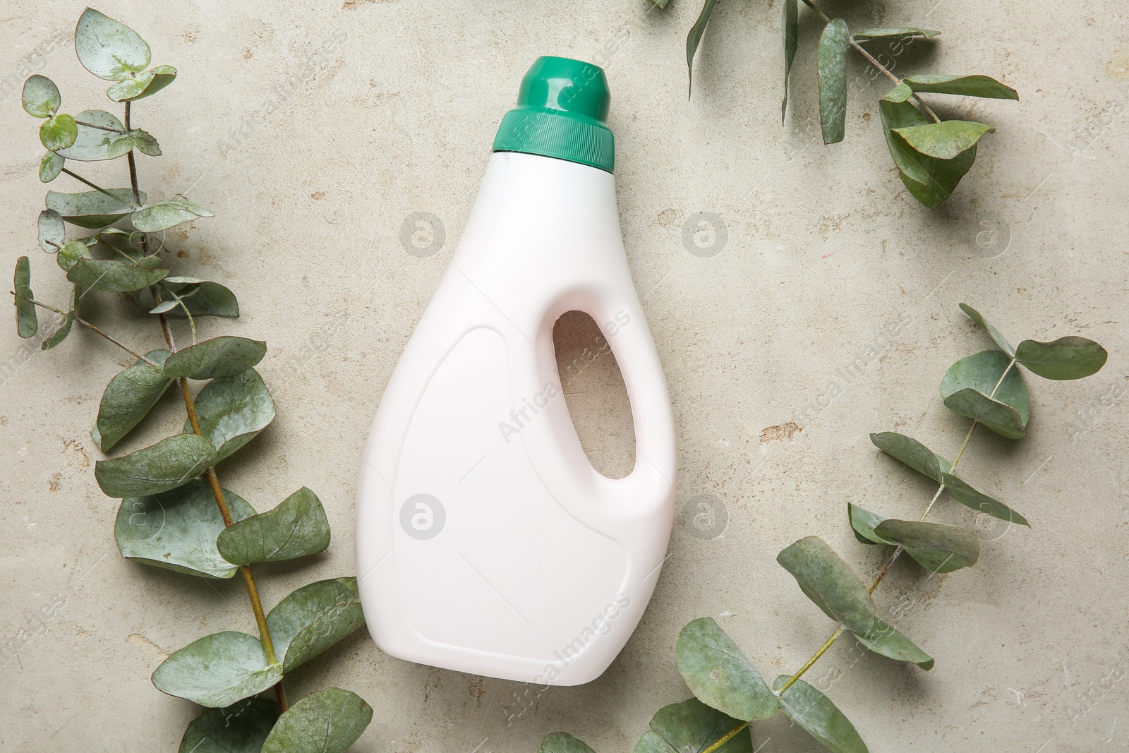 Photo of Laundry detergent in bottle among eucalyptus branches on grey textured table, flat lay