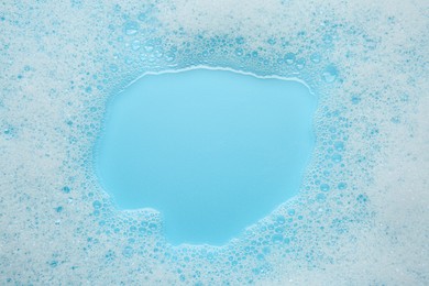 Washing laundry. White foam with bubbles on light blue background, top view