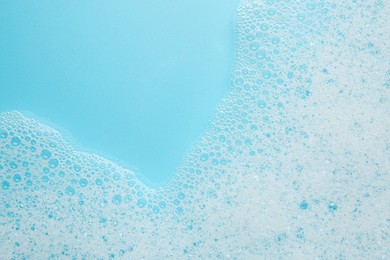 Photo of Washing laundry. White foam with bubbles on light blue background, top view. Space for text