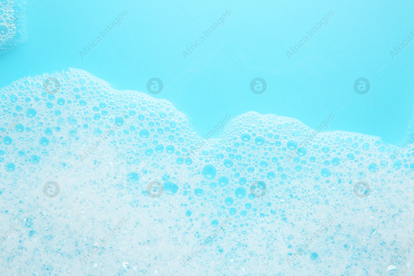 Photo of Washing laundry. White foam with bubbles on light blue background, top view. Space for text