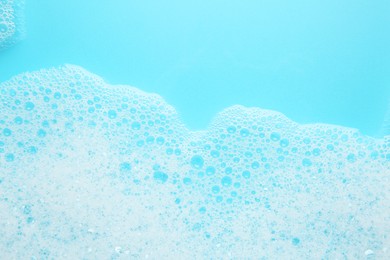 Photo of Washing laundry. White foam with bubbles on light blue background, top view. Space for text