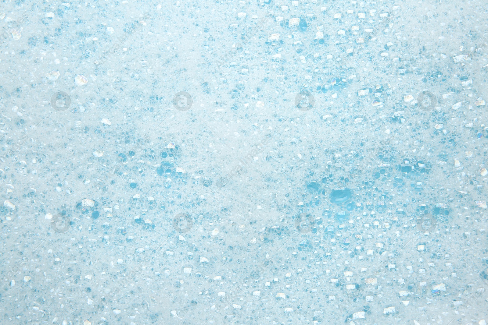 Photo of Washing laundry. White foam with bubbles on light blue background, top view