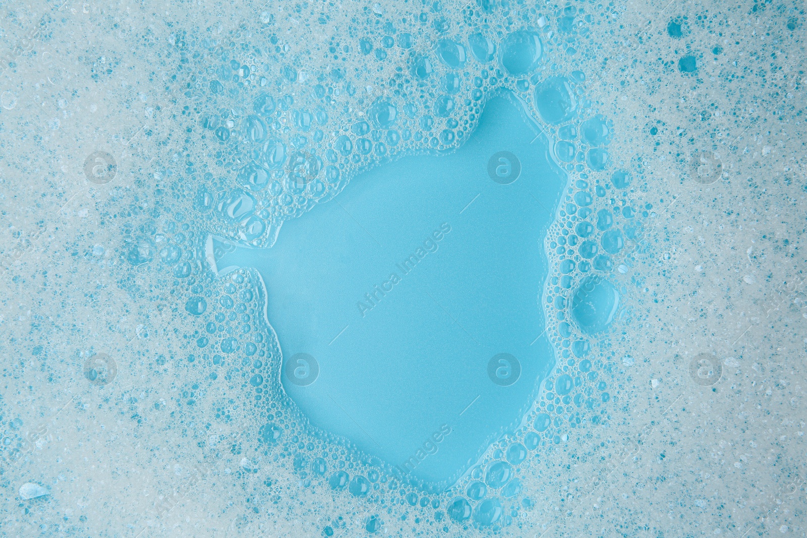 Photo of Washing laundry. White foam with bubbles on light blue background, top view