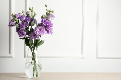 Vase with beautiful eustoma flowers on wooden table, space for text