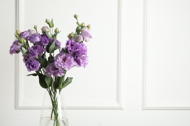 Vase with beautiful eustoma flowers near white wall, space for text