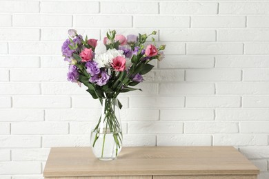 Vase with beautiful eustoma flowers on wooden chest of drawers, space for text