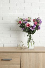 Vase with beautiful eustoma flowers on wooden chest of drawers