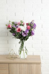 Vase with beautiful eustoma flowers on wooden chest of drawers