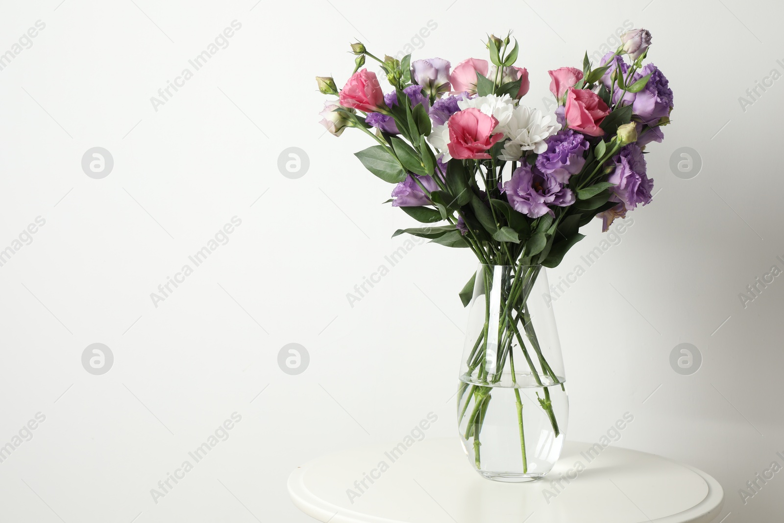 Photo of Vase with beautiful eustoma flowers on white table, space for text