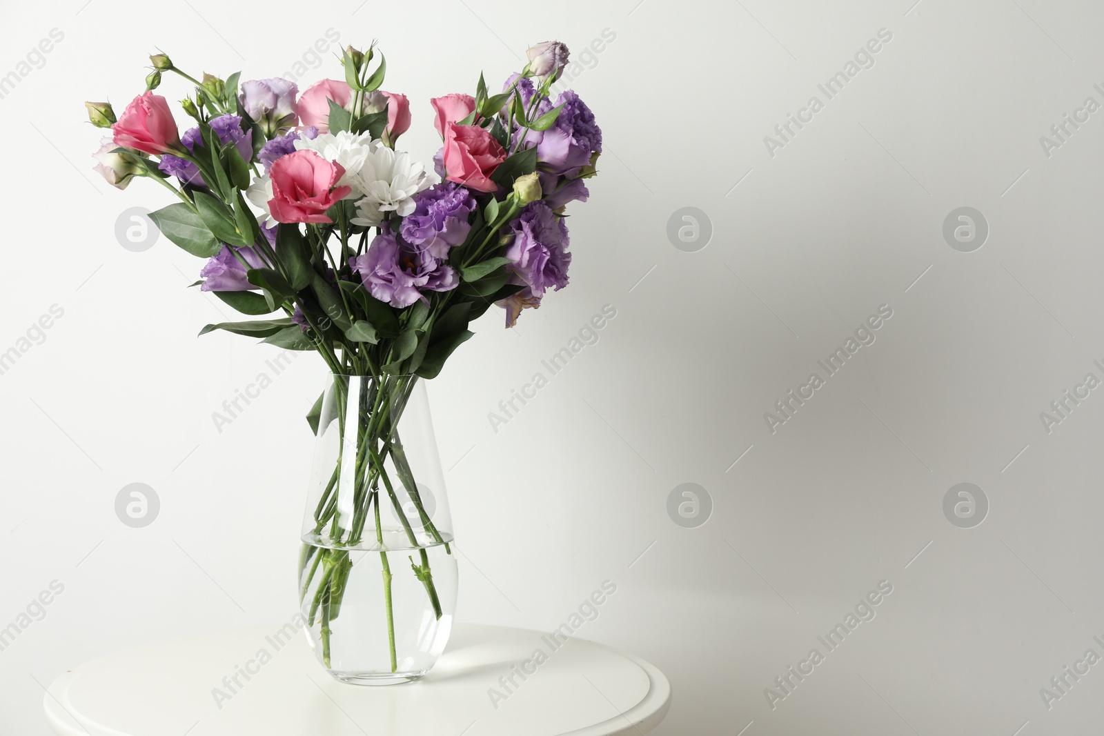 Photo of Vase with beautiful eustoma flowers on white table, space for text