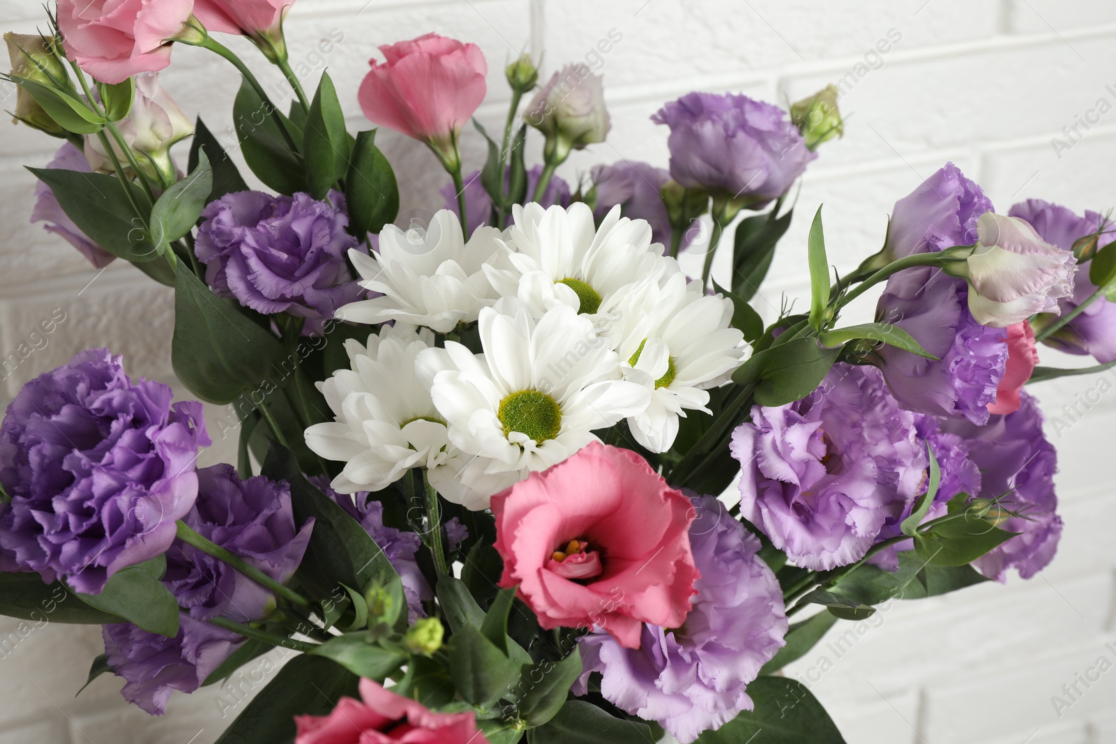 Photo of Vase with beautiful eustoma flowers near white brick wall, closeup