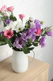 Vase with beautiful eustoma flowers on wooden chest of drawers