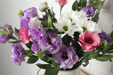 Photo of Vase with beautiful eustoma flowers near white brick wall, closeup