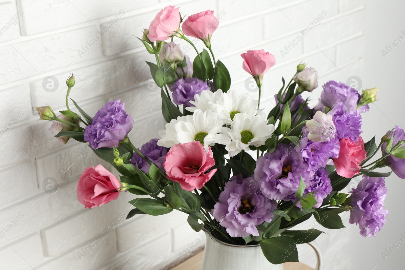 Photo of Vase with beautiful eustoma flowers near white brick wall, closeup