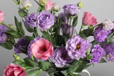 Photo of Vase with beautiful eustoma flowers near light grey wall, closeup