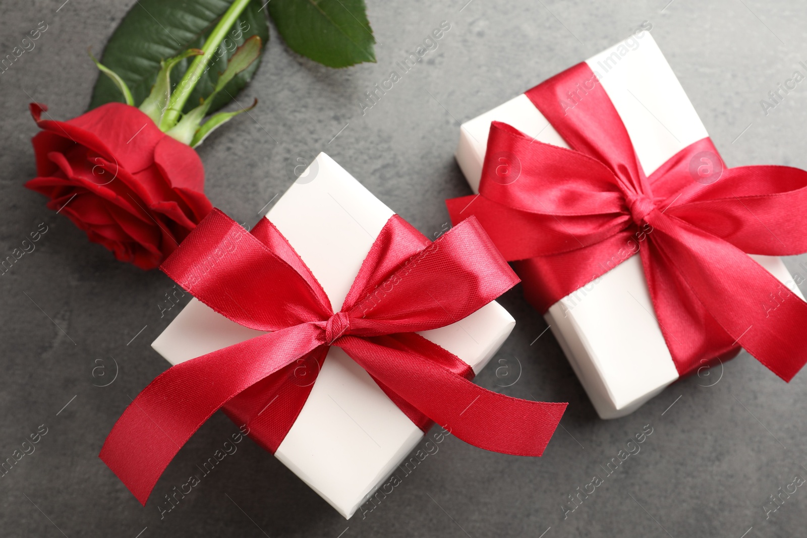 Photo of Gift boxes with bows and rose on grey table, flat lay