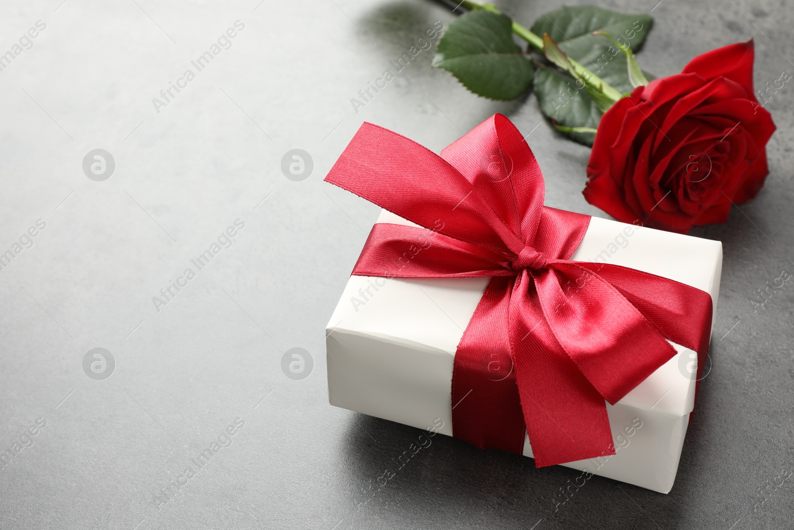 Photo of Gift box with bow and rose on grey table, space for text