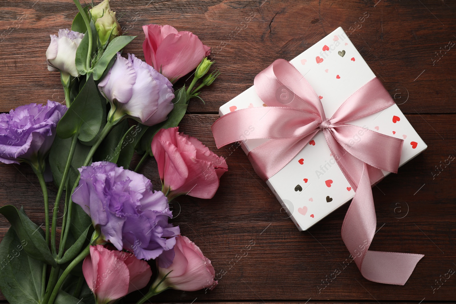 Photo of Gift box with bow and flowers on wooden table, flat lay