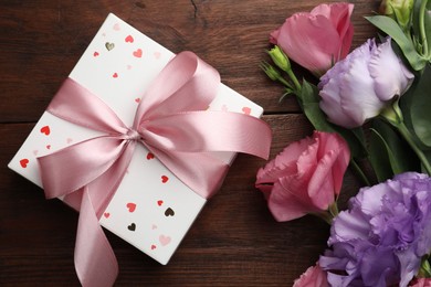 Photo of Gift box with bow and flowers on wooden table, flat lay