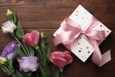 Gift box with bow and flowers on wooden table, flat lay