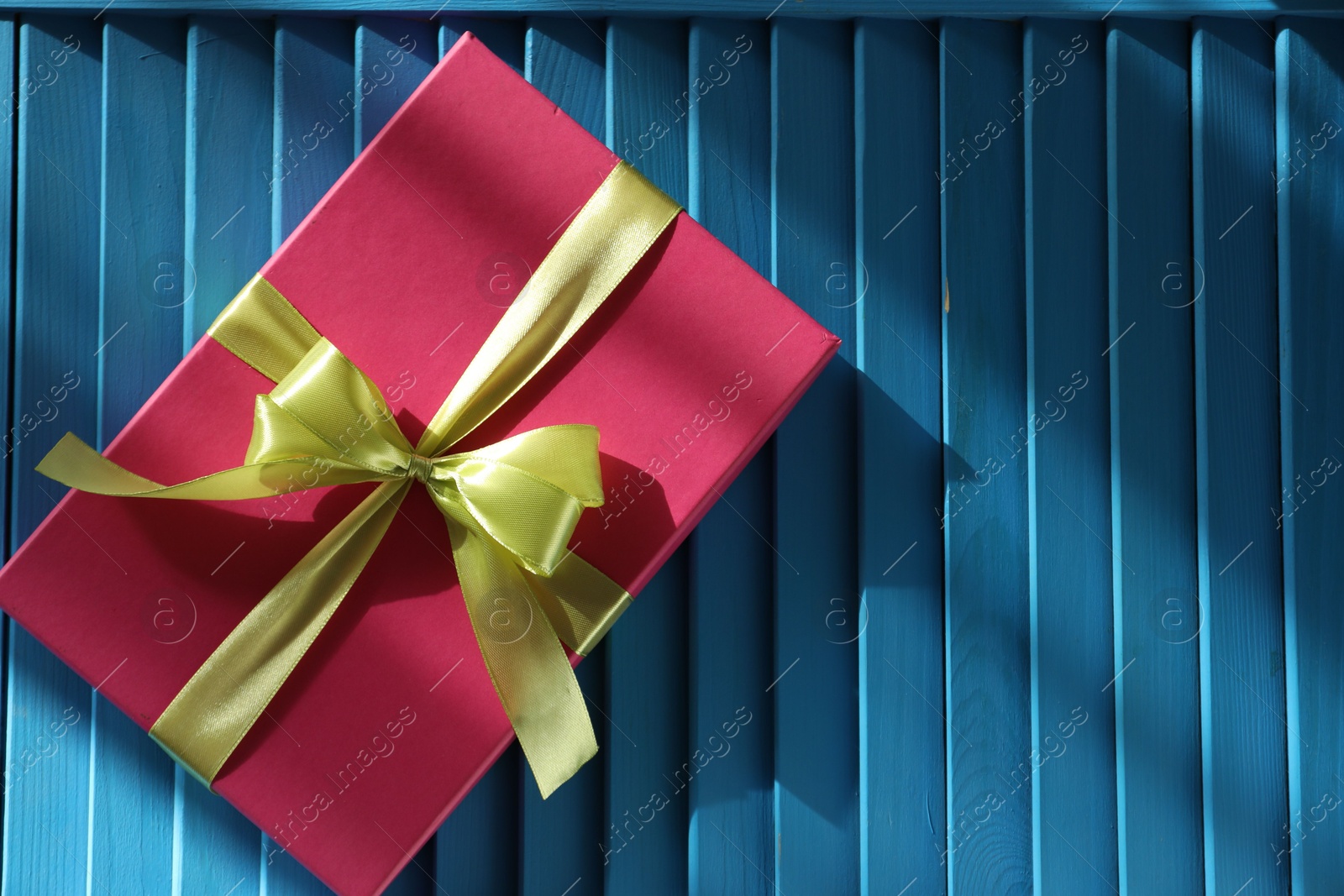 Photo of Gift box with bow on blue textured table, top view. Space for text