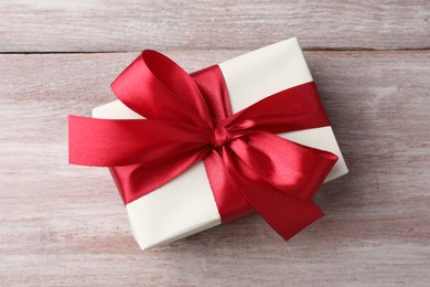 Gift box with bow on pink wooden table, top view