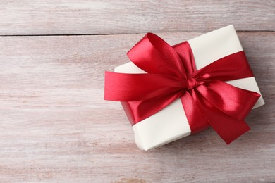 Photo of Gift box with bow on pink wooden table, top view. Space for text