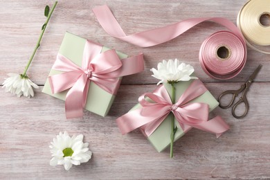 Photo of Gift boxes with bows, ribbon, scissors and flowers on pink wooden table, flat lay