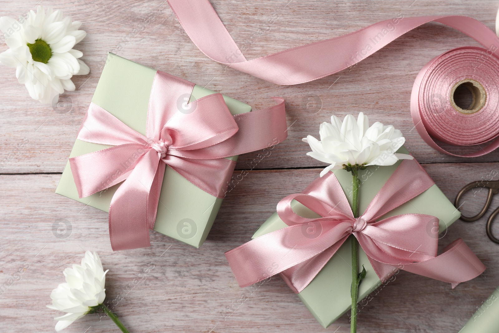 Photo of Gift boxes with bows, ribbon, scissors and flowers on pink wooden table, flat lay