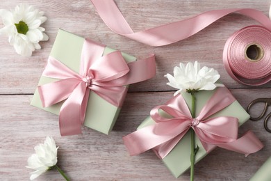 Photo of Gift boxes with bows, ribbon, scissors and flowers on pink wooden table, flat lay