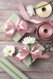 Gift boxes with bows, ribbon, scissors and flowers on pink wooden table, flat lay