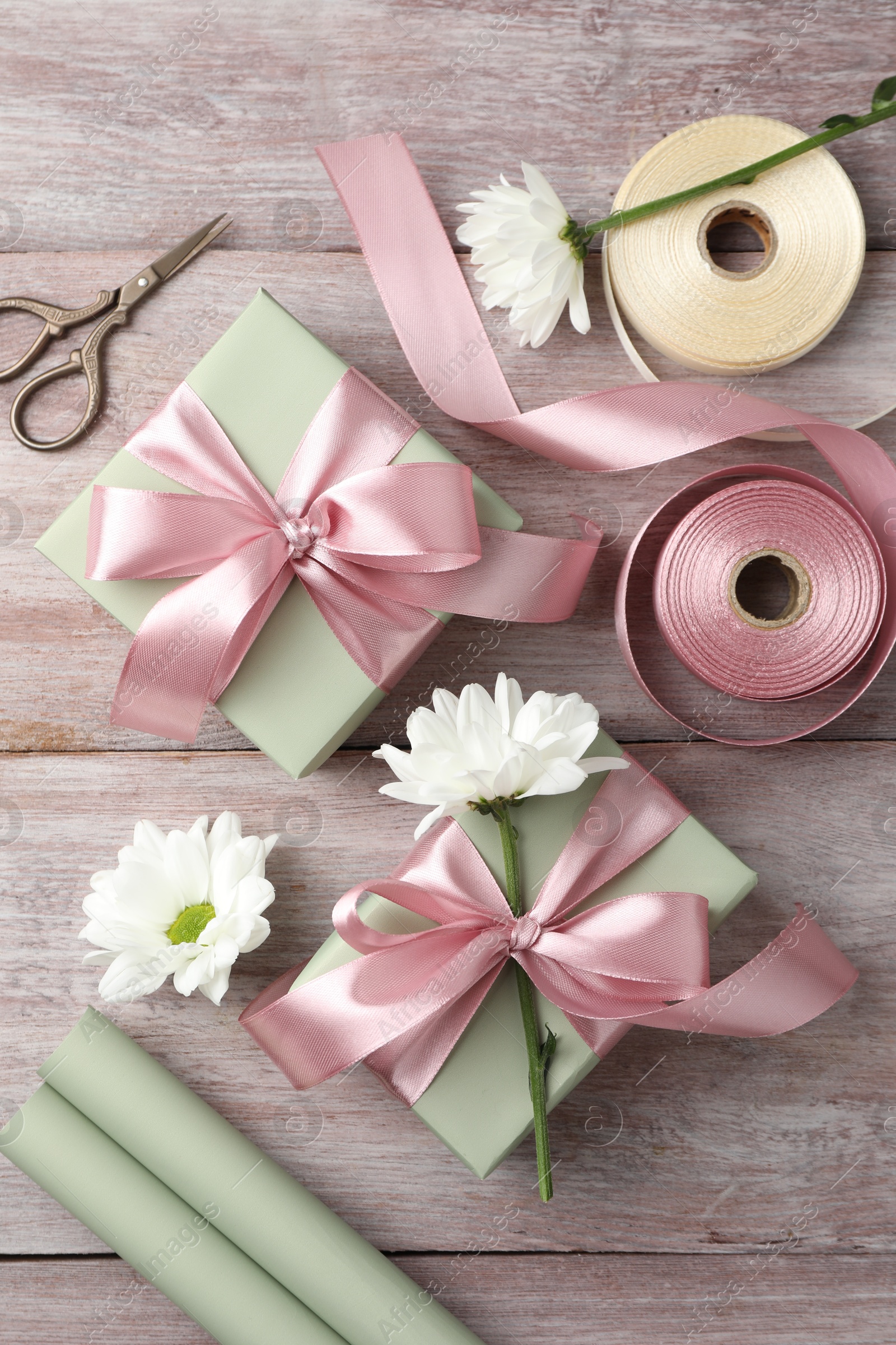 Photo of Gift boxes with bows, ribbon, scissors and flowers on pink wooden table, flat lay