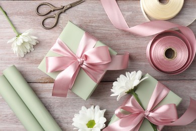 Photo of Gift boxes with bows, ribbon, scissors and flowers on pink wooden table, flat lay