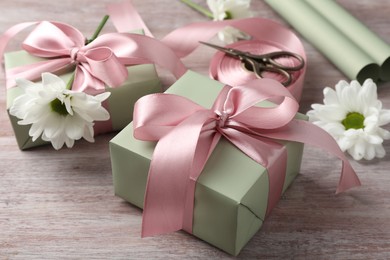 Photo of Gift boxes with bows, ribbon, scissors and flowers on pink wooden table, closeup