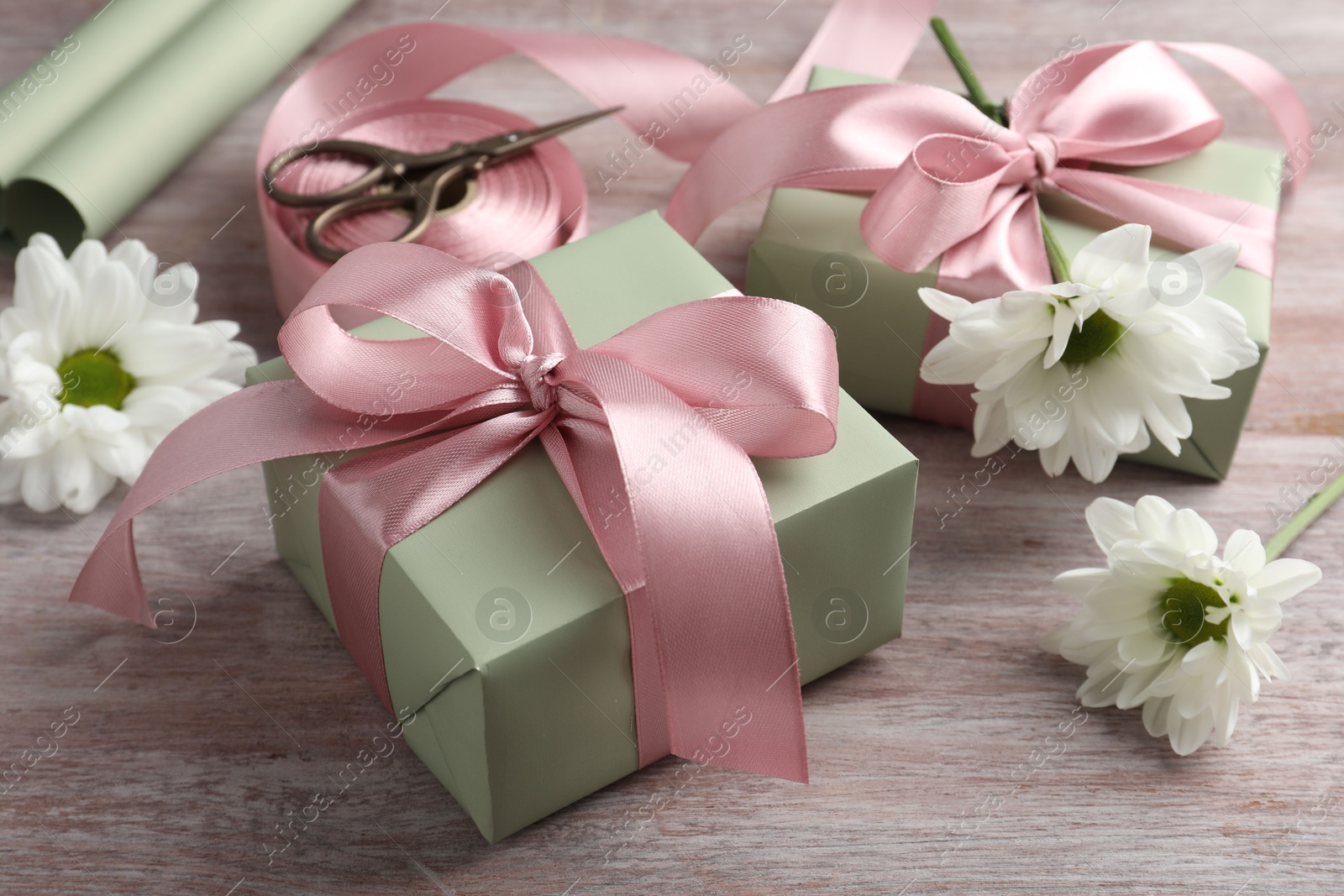 Photo of Gift boxes with bows, ribbon, scissors and flowers on pink wooden table, closeup