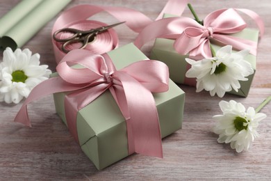 Photo of Gift boxes with bows, ribbon, scissors and flowers on pink wooden table, closeup