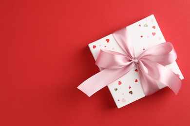 Gift box with bow on red background, top view. Space for text