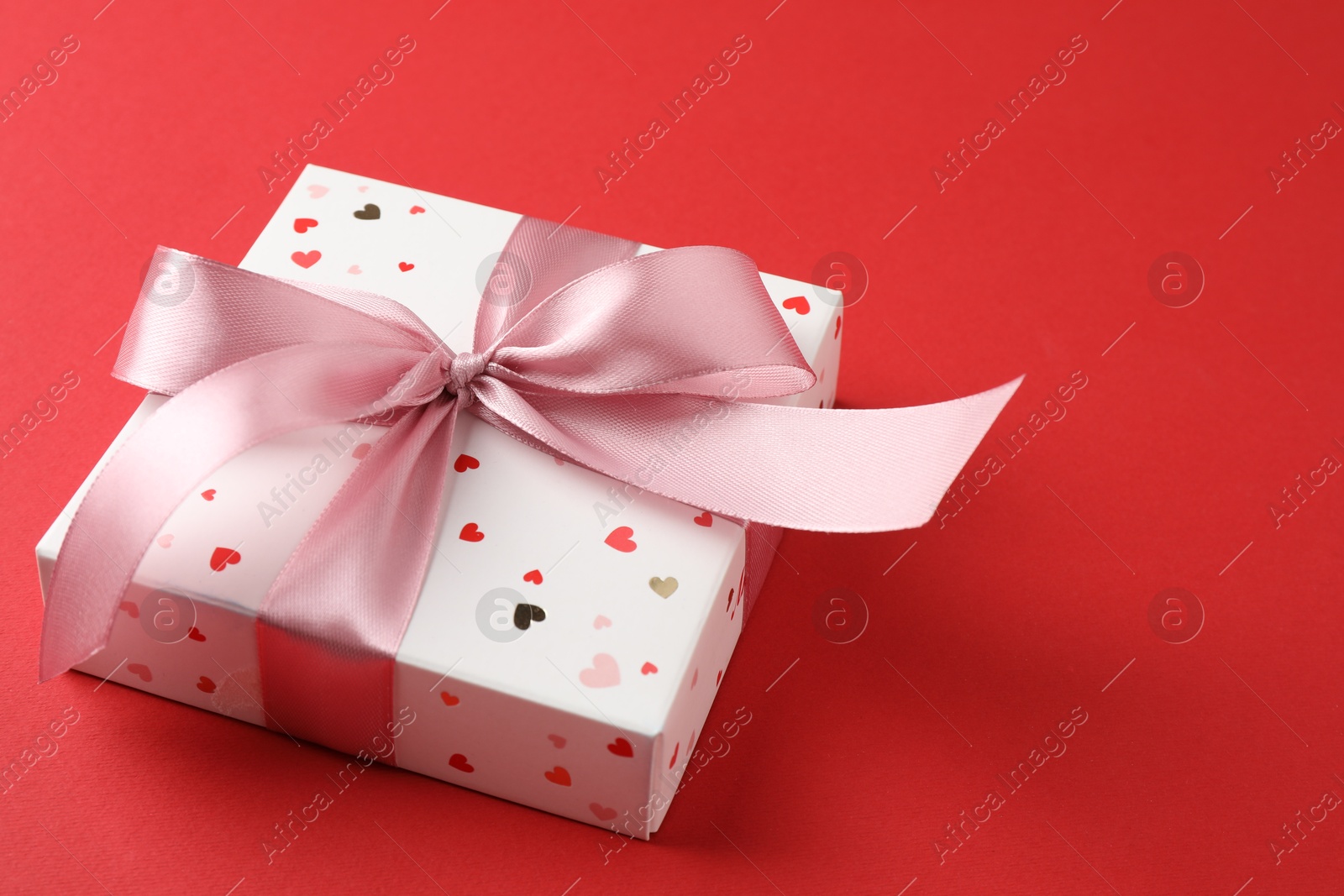 Photo of Gift box with bow on red background, space for text