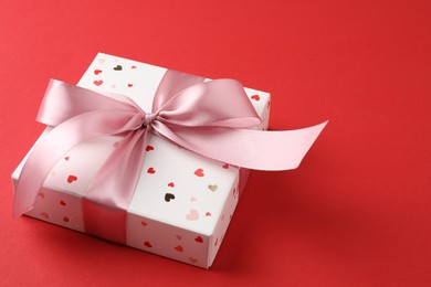 Gift box with bow on red background, space for text