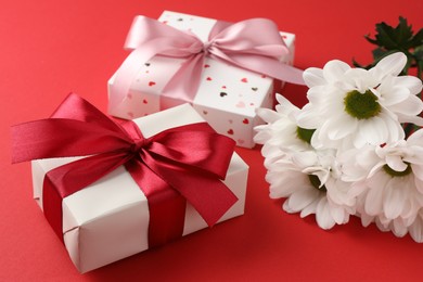 Photo of Gift boxes with bows and flowers on red background